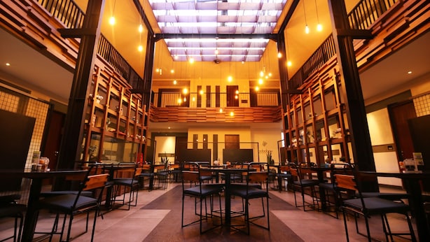 A spacious indoor area with multiple tables and chairs, wooden bookshelves, and a high ceiling with a skylight. - Hotel Nyland Cipaganti (Bandung)