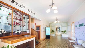A reception area with a wooden counter, a reception desk, a sign for 'The Manly Motel', and a 'Weekend Sessions' digital display. - Nightcap at Manly Hotel (Manly)