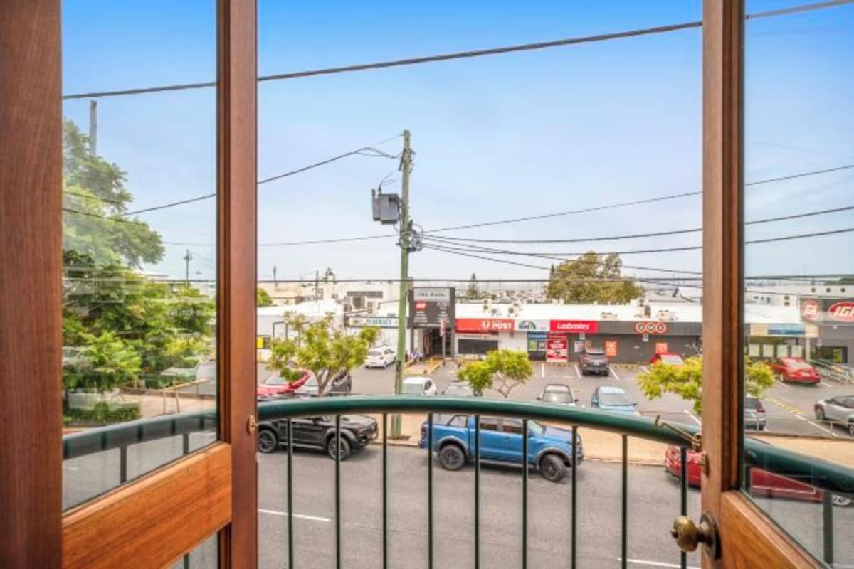 A view from a balcony with a metal railing, overlooking a street with cars and buildings, including a visible 'POST' sign.