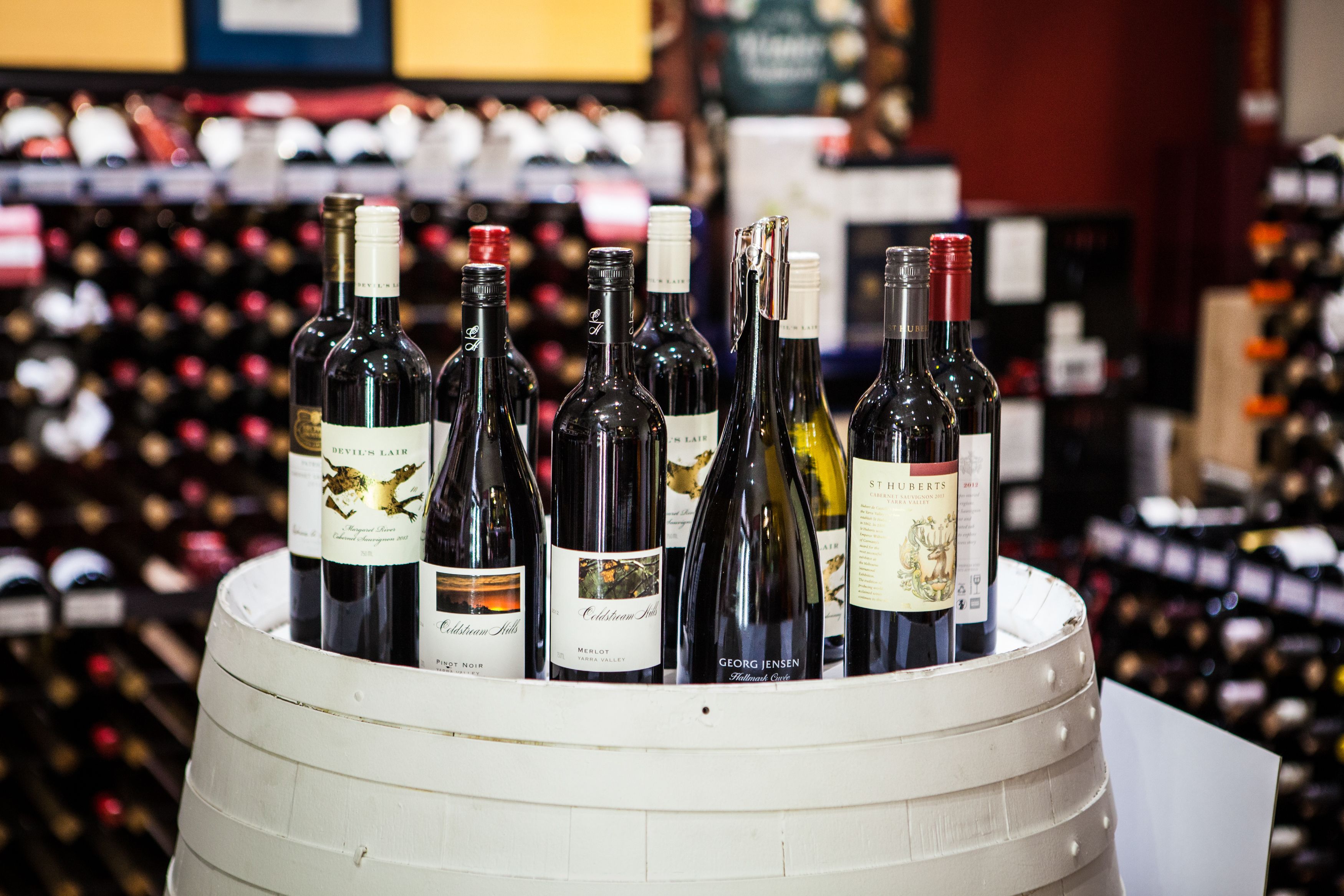 Variedade de garrafas de vinho em um barril, com estantes de vinho ao fundo.