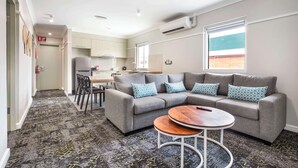 A modern living room with a grey sectional sofa, a round coffee table, and a kitchen in the background. - Nightcap at Manly Hotel (Manly)
