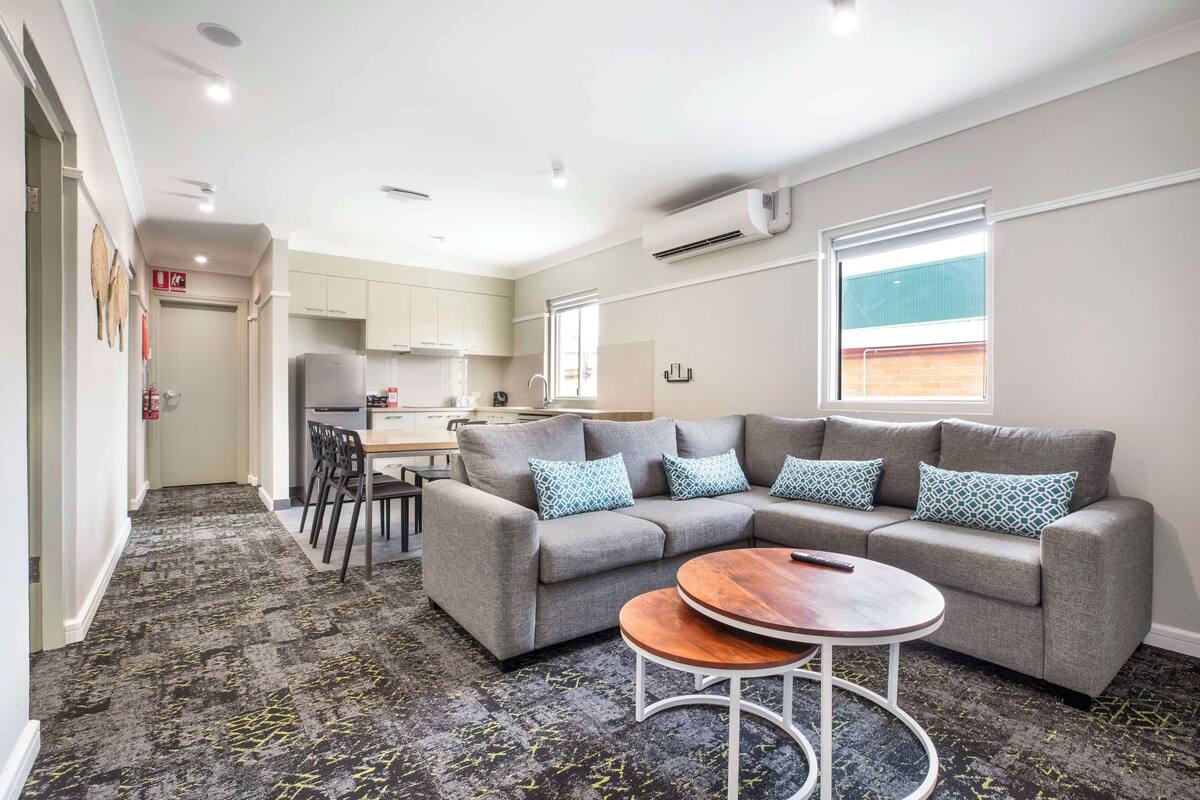 A modern living room with a grey sectional sofa, a round coffee table, and a kitchen in the background.