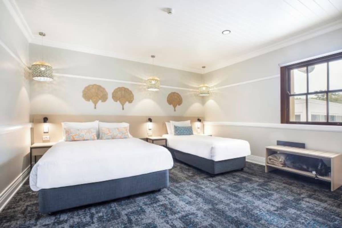 A hotel room with two beds, a large window, and wall-mounted lamps.