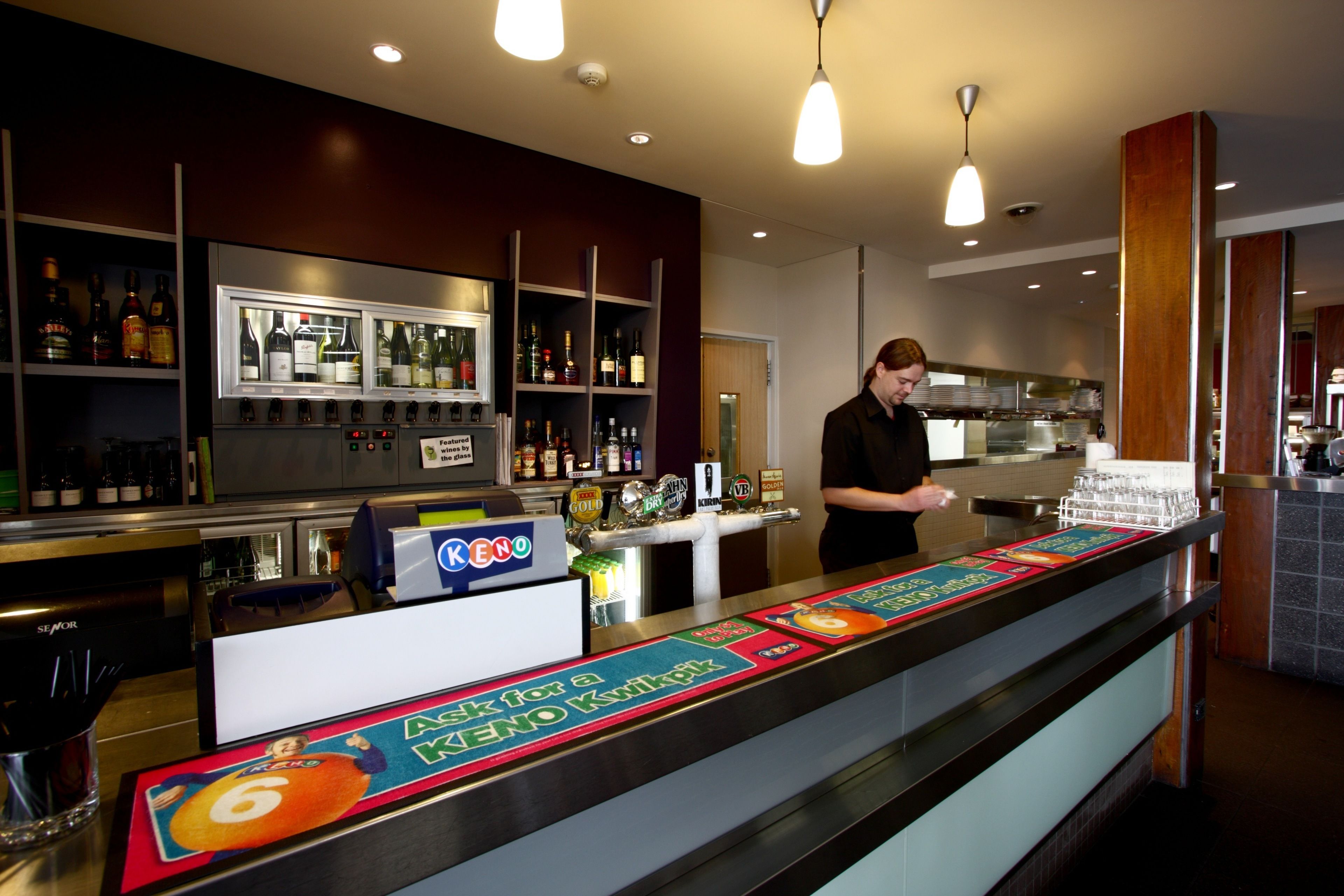 A bar area with a counter, shelves with bottles, and a person standing behind the counter.