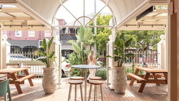 An outdoor patio with wooden tables and chairs, surrounded by potted plants, under a white canopy structure. - Nightcap at Manly Hotel (Manly)