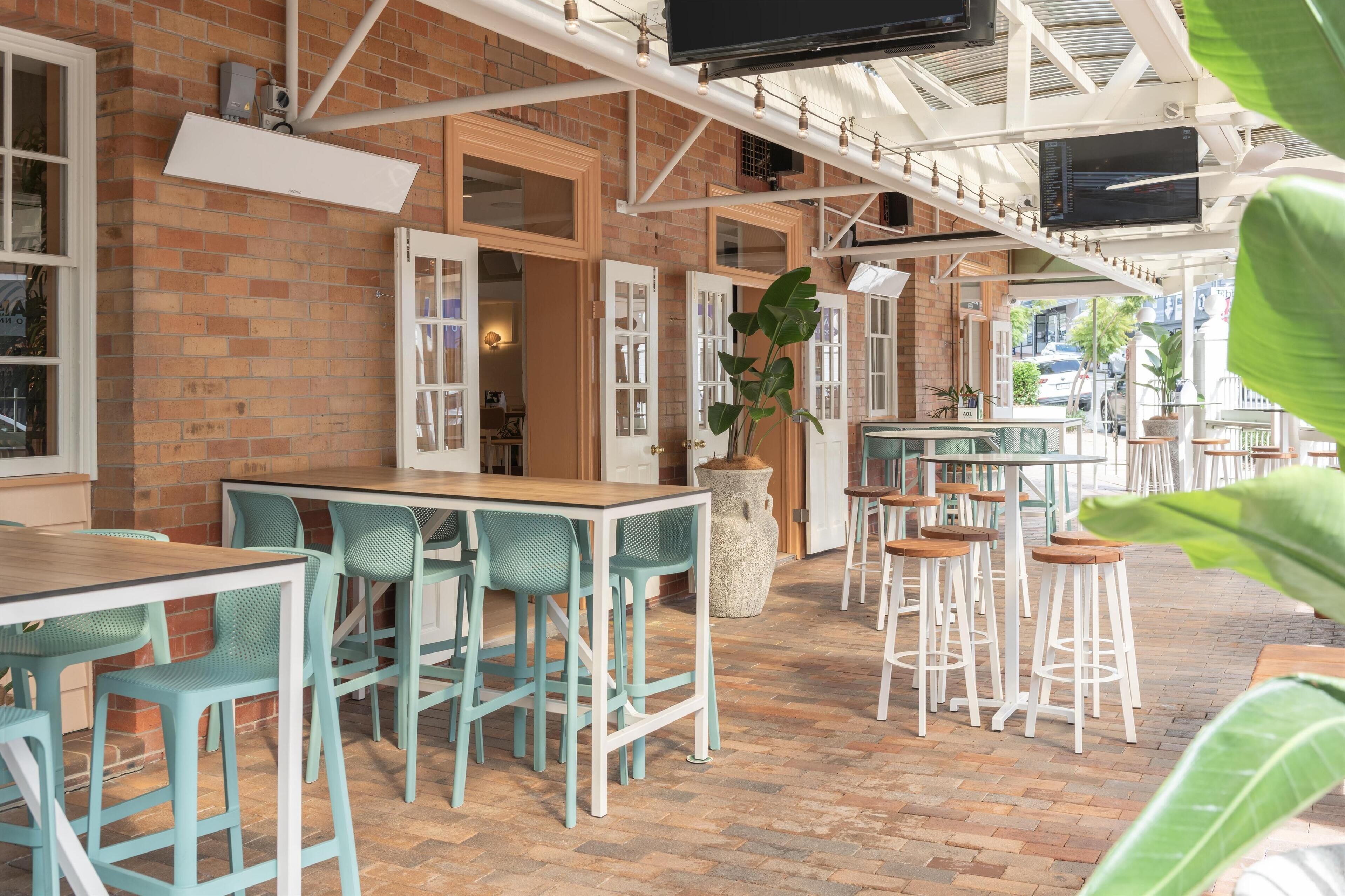 An outdoor café with brick walls, white-framed windows, and green metal chairs.