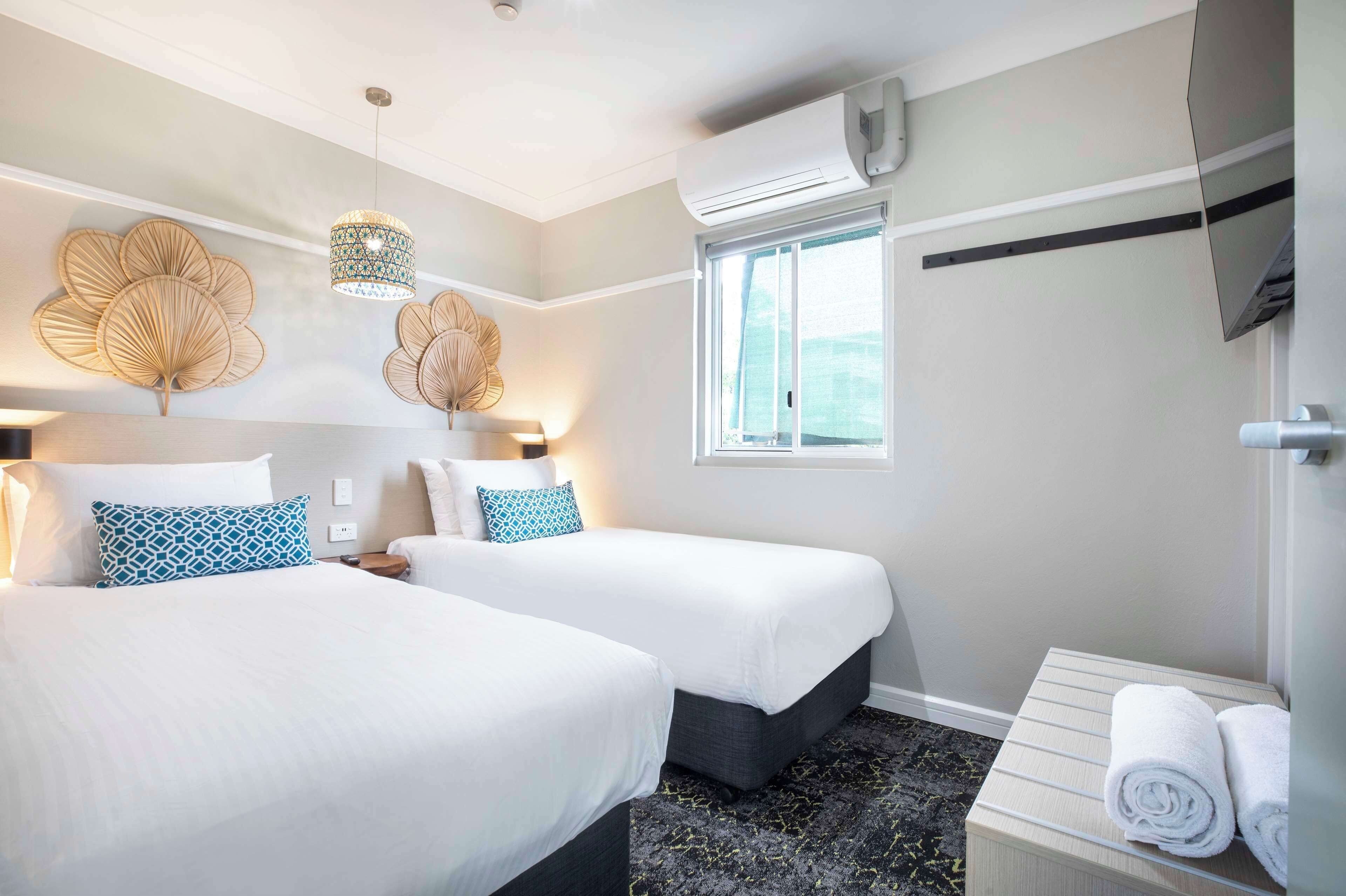 Habitación de hotel con dos camas, una ventana con cortinas, aire acondicionado de pared y una mesita con toallas.