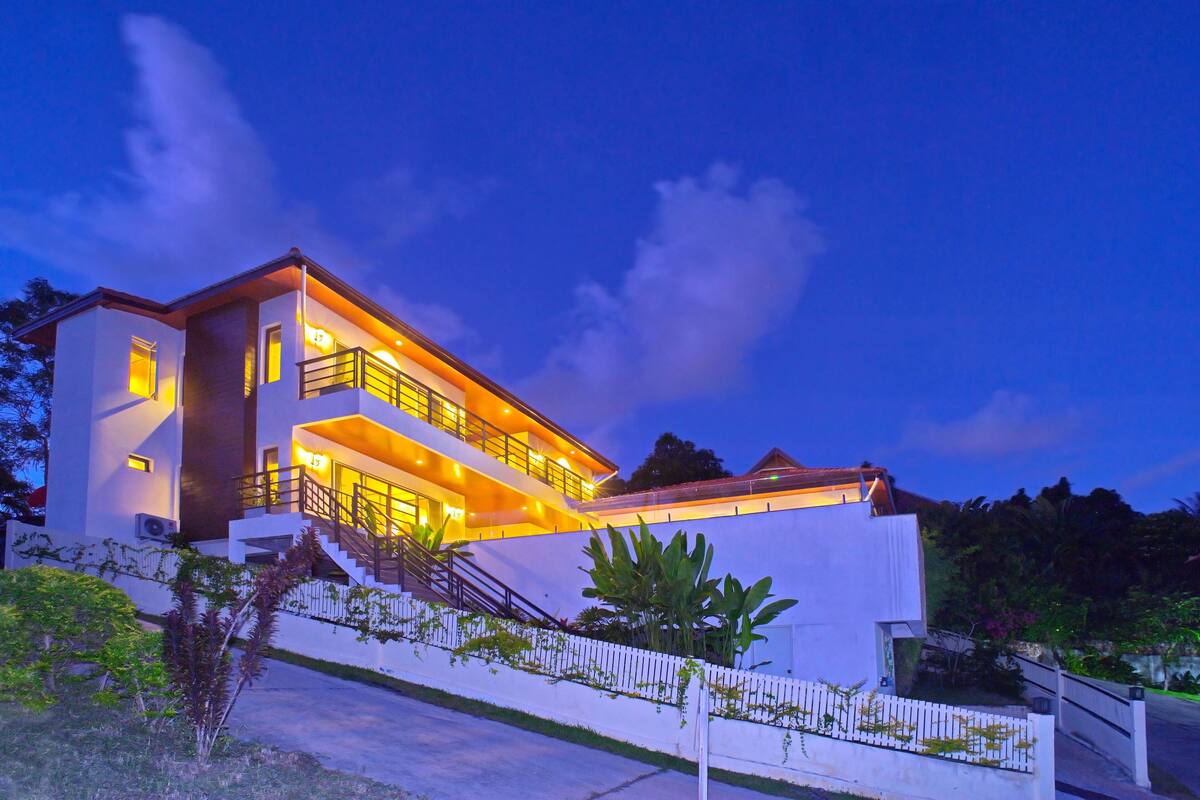 A modern two-story house with a balcony, a staircase, and a white fence.
