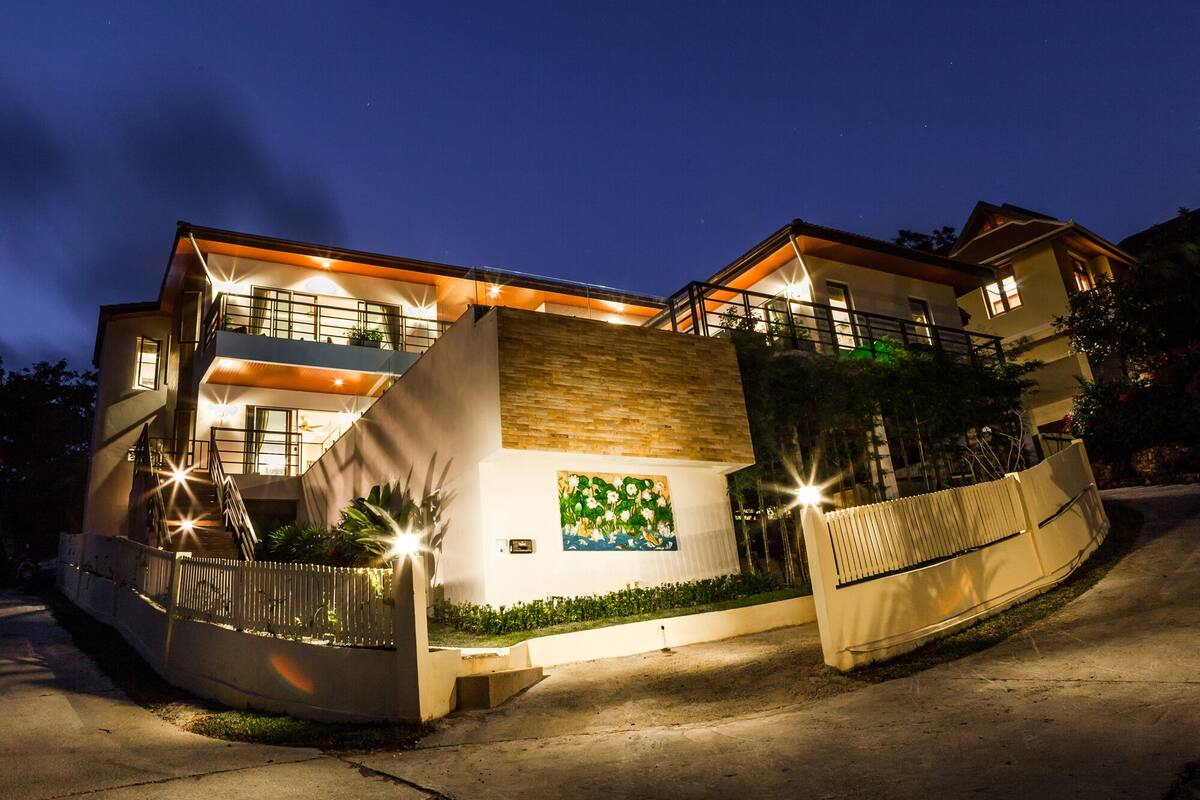 A modern two-story house with a balcony, a garden, and a large window with a floral design.