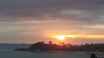 A coastal sunset view with a small island, palm trees, and a boat in the water.
