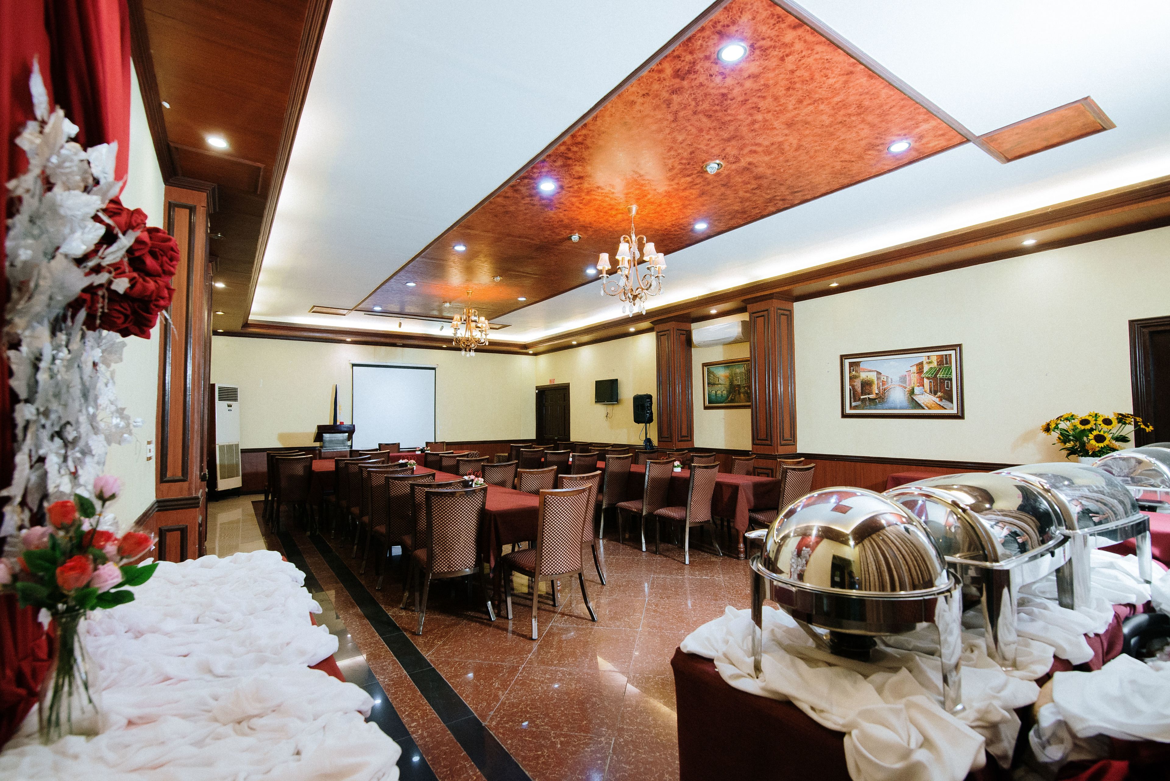 Un salón de banquetes con mesas, sillas, una pantalla de proyector y servicio de buffet.