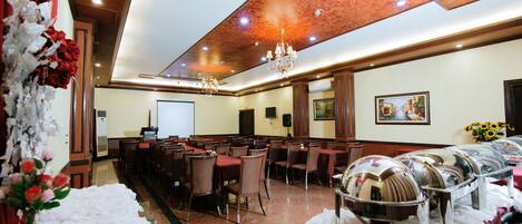 Un salón de banquetes con mesas, sillas, una pantalla de proyector y servicio de buffet.
