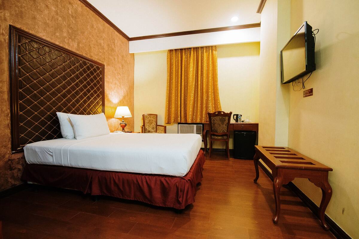A hotel room with a large bed, a desk with a chair, a television mounted on the wall, and a small table.