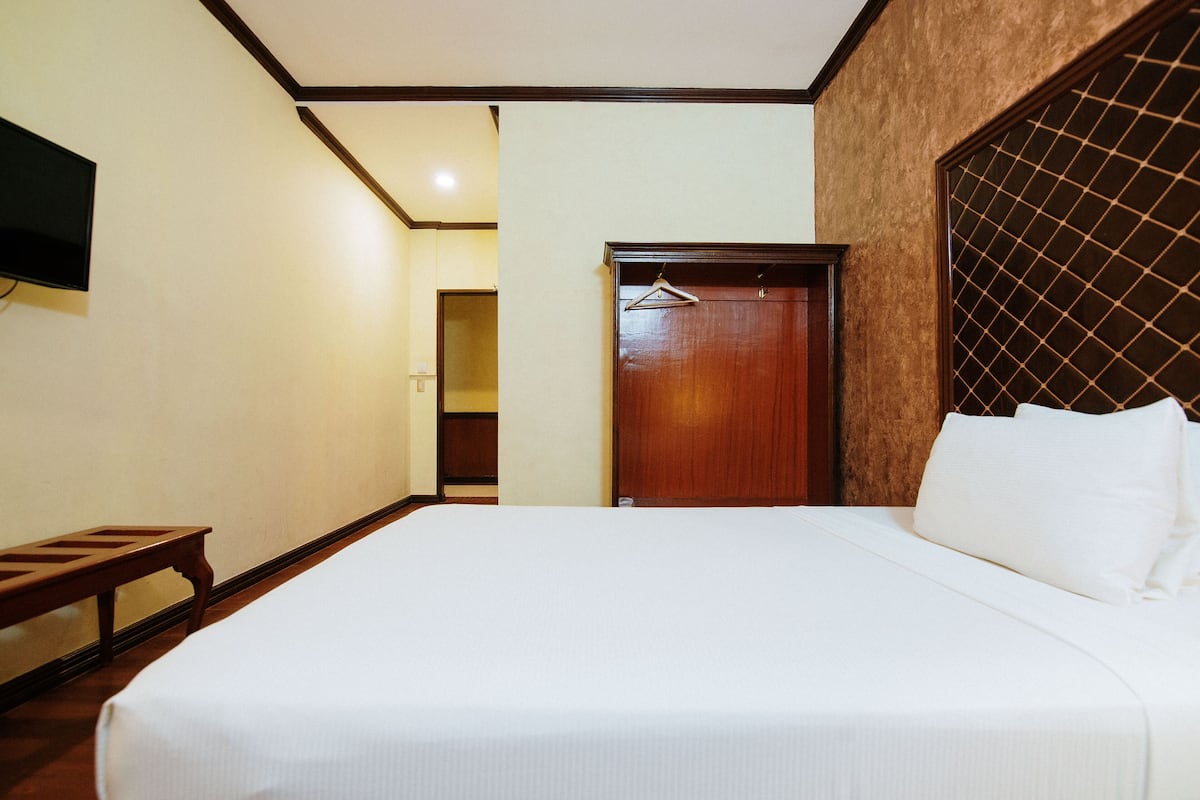A hotel room with a large bed, a wooden headboard, a wardrobe, and a television mounted on the wall.