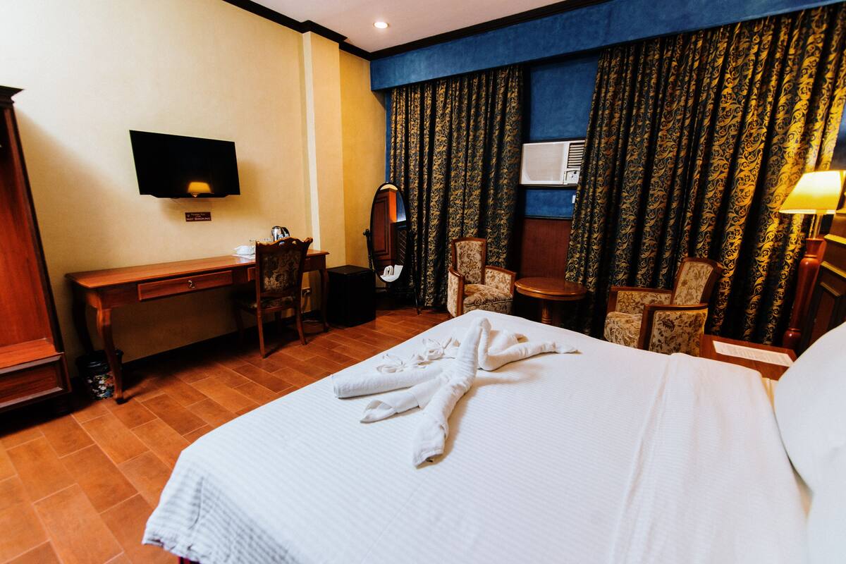A hotel room with a bed, a desk, a chair, a television, and a window with curtains.