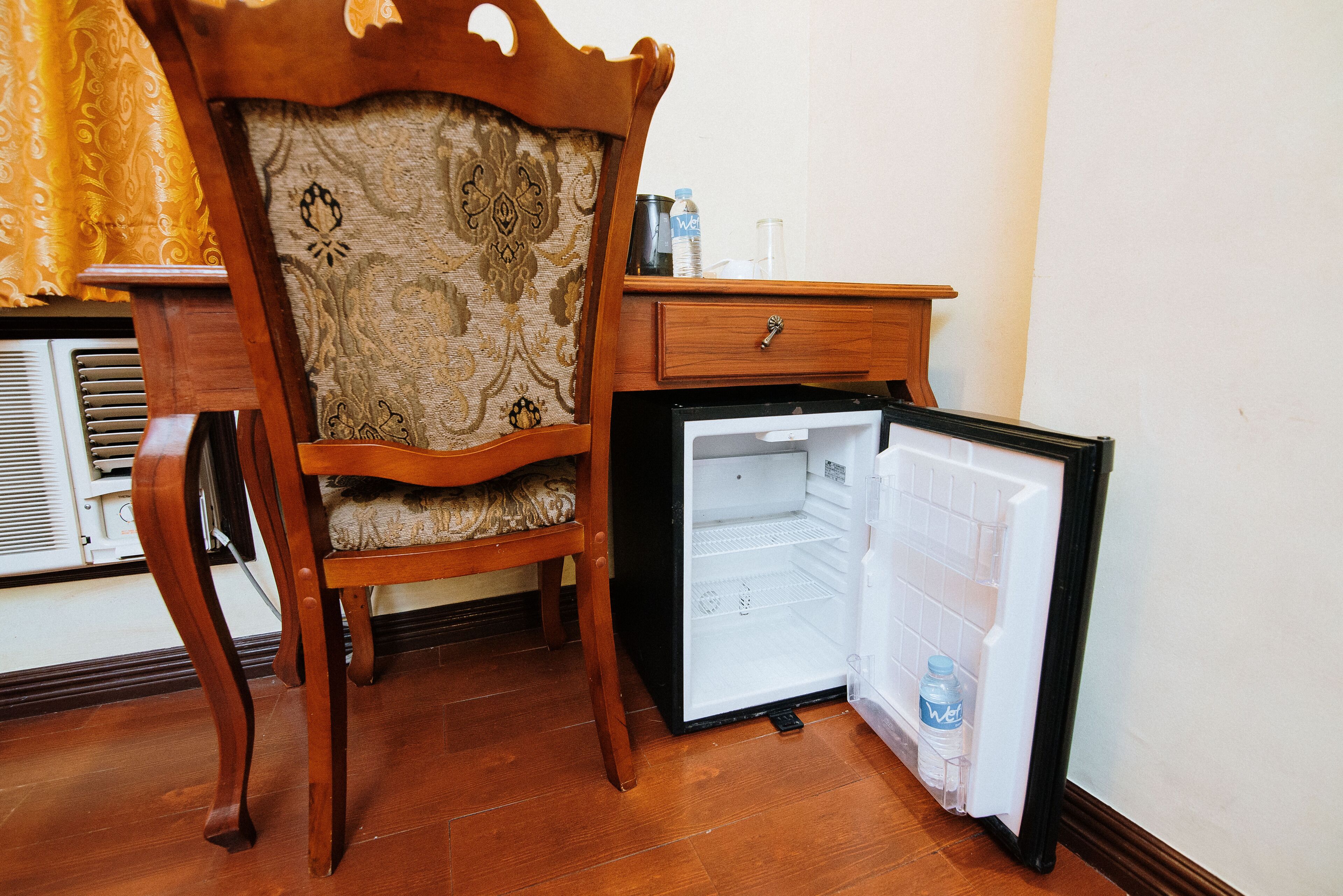 Une petite pièce comprenant une chaise en bois, une petite table en bois et un mini-réfrigérateur.