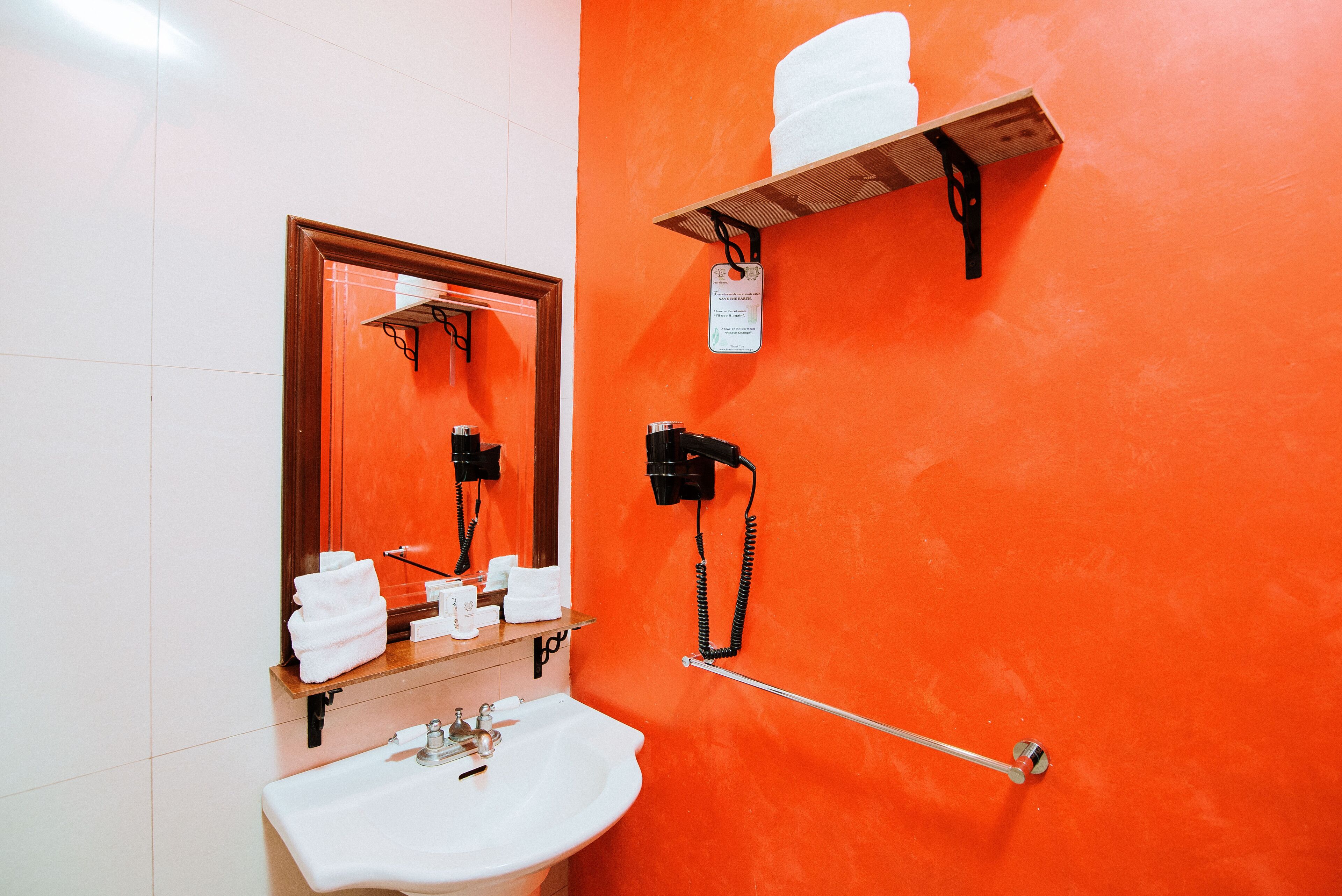 Un bagno con un lavandino bianco, uno specchio, un asciugacapelli e un porta asciugamani.