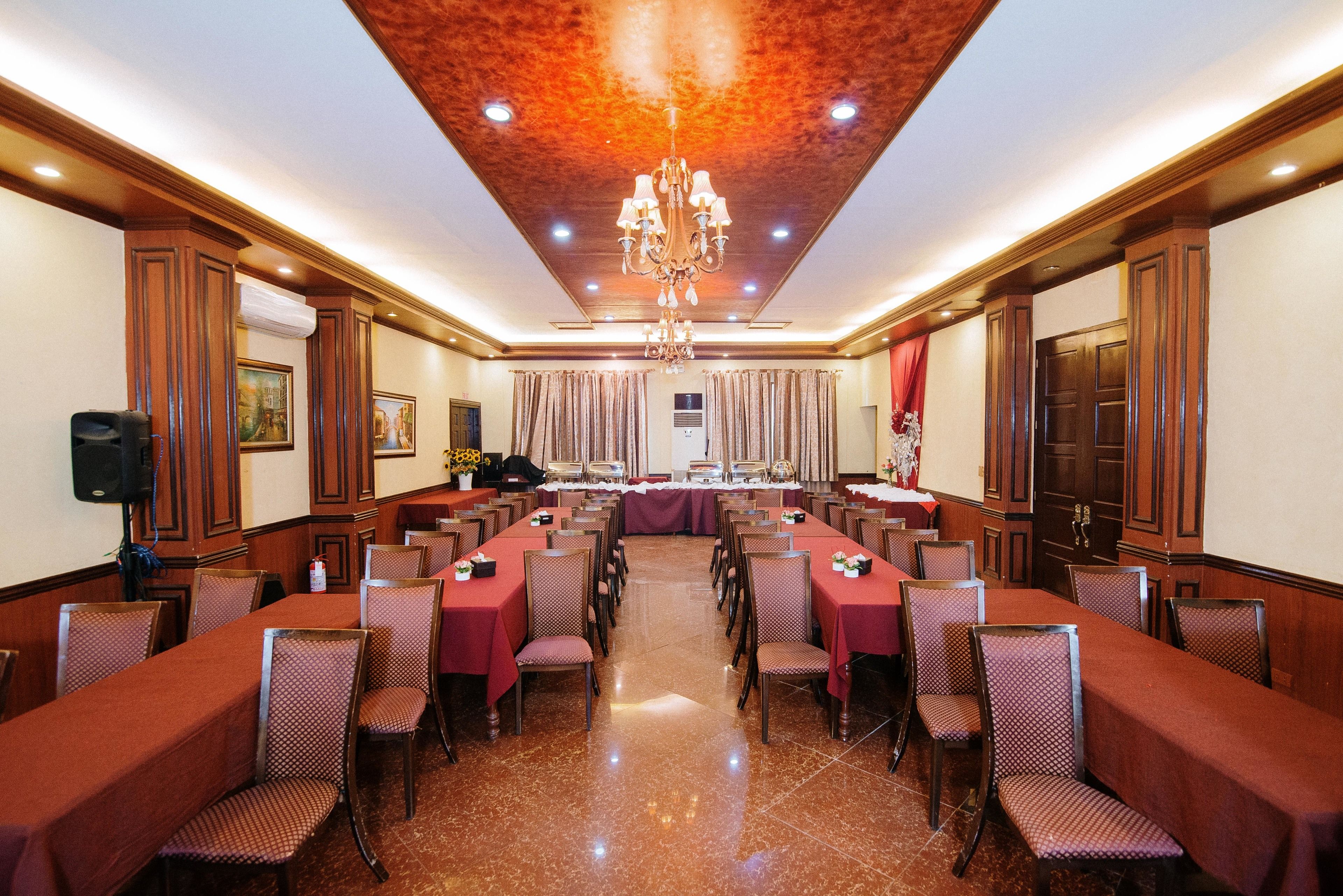 A conference room with a long table, multiple chairs, a chandelier, and a red curtain backdrop.