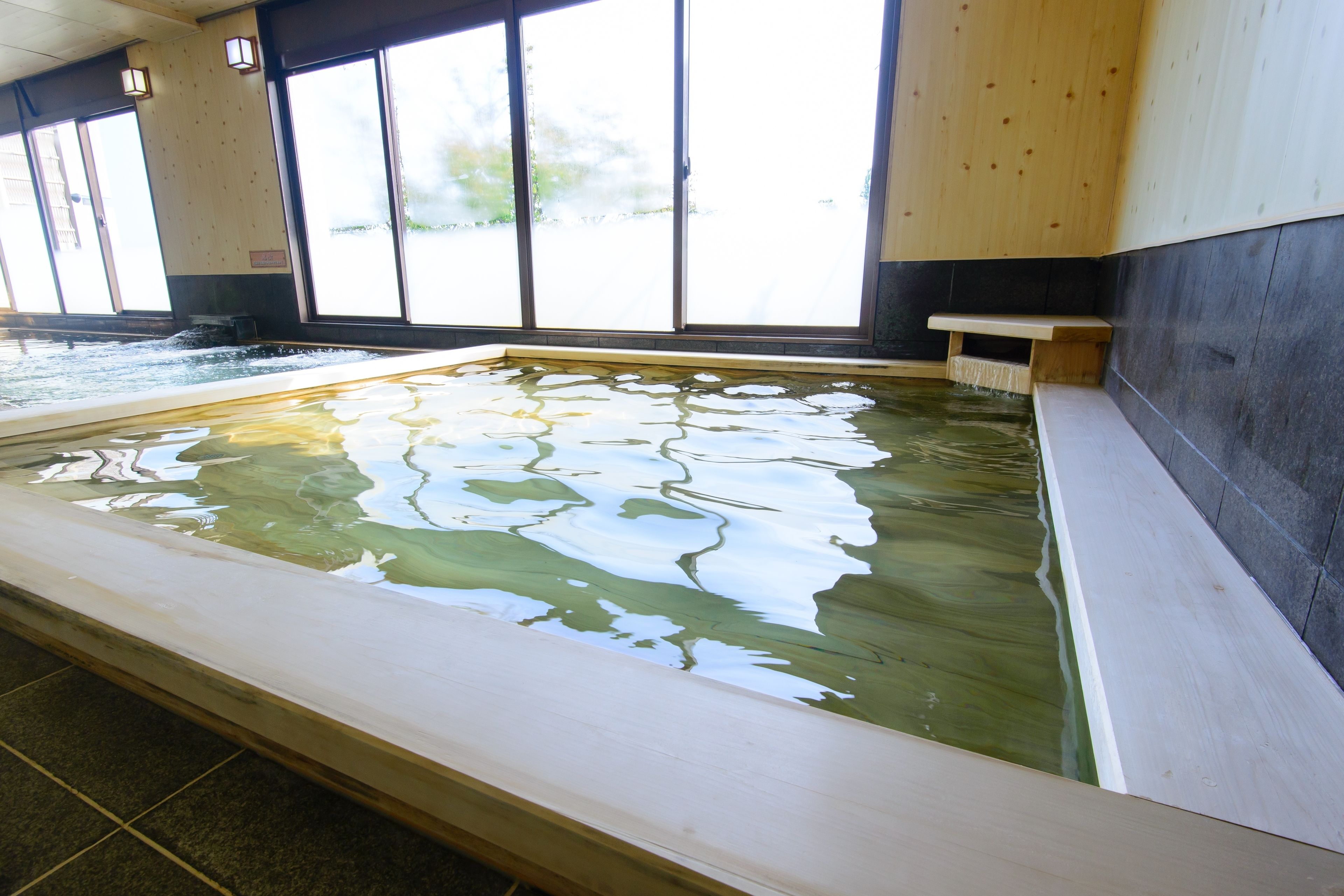 Een groot binnenzwembad met warm water en een houten bank langs de rand.