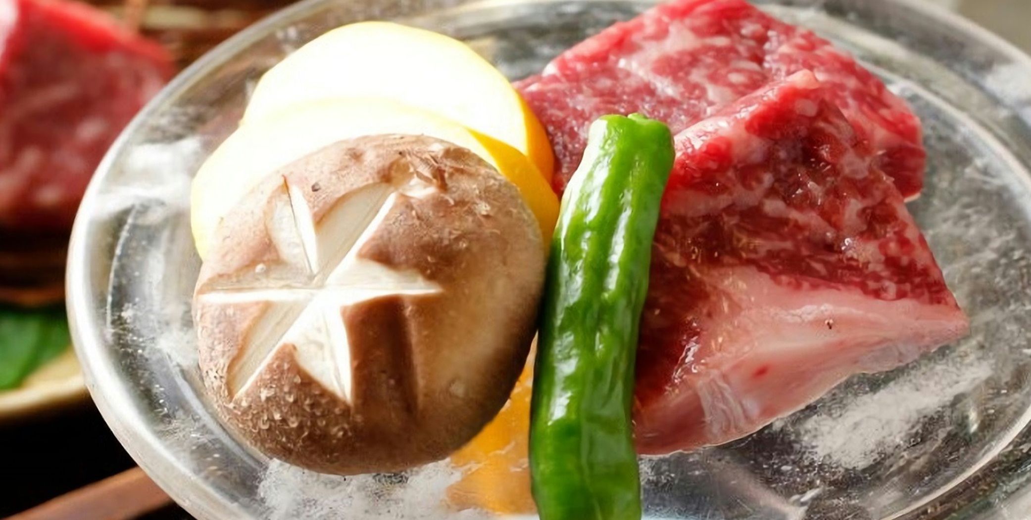 Une assiette avec des tranches de viande, un champignon et un piment vert.