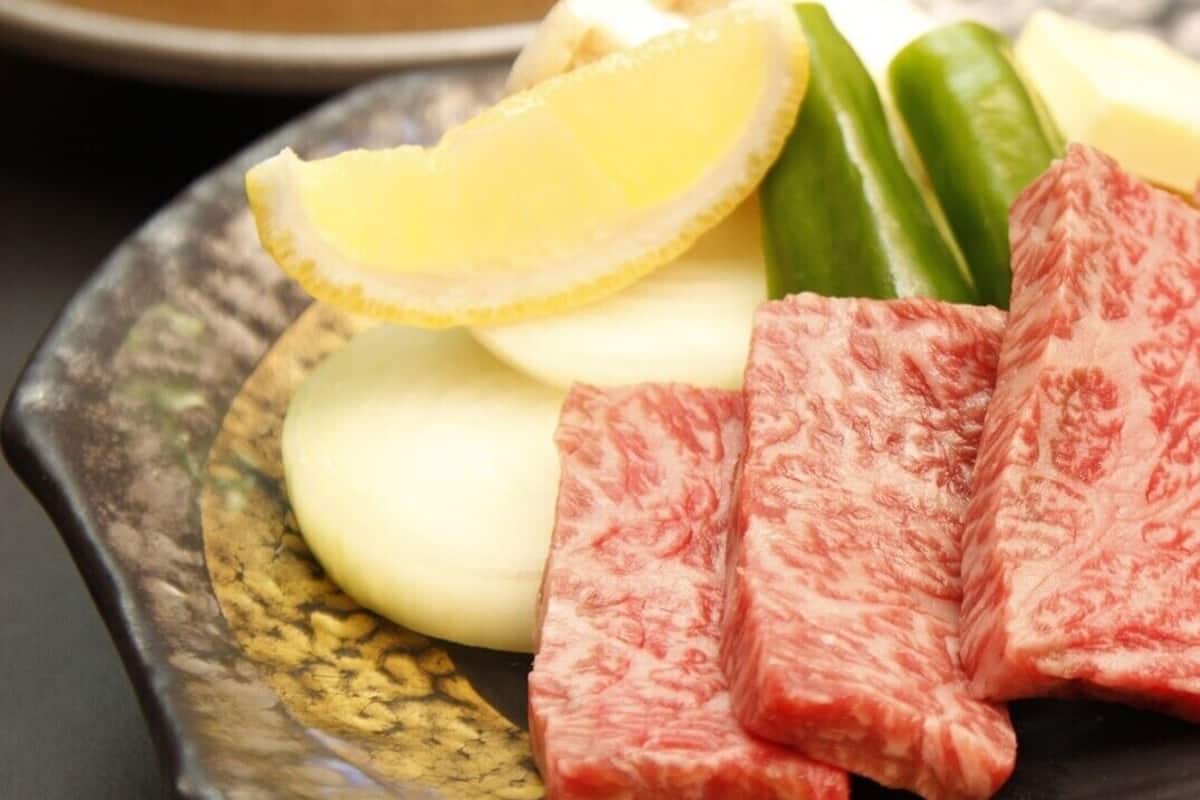 Um prato com carne fatiada, um limão e pimentões verdes.