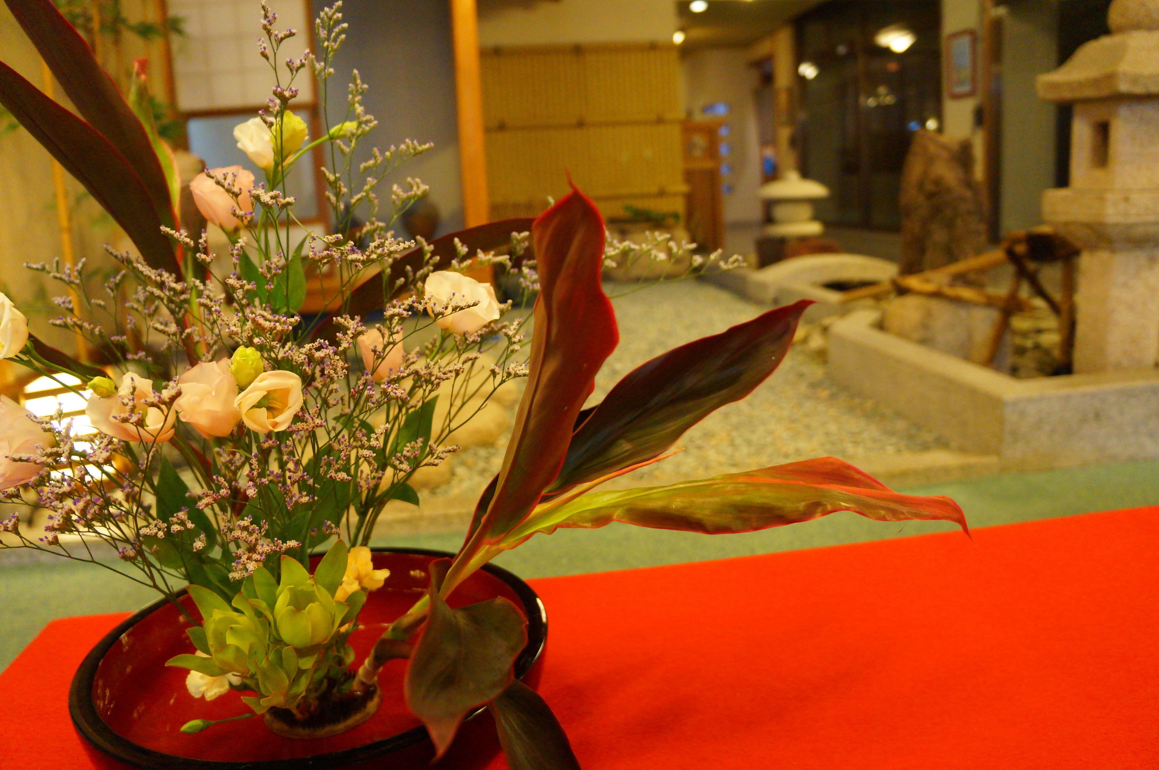 A red vase with a floral arrangement on a table.