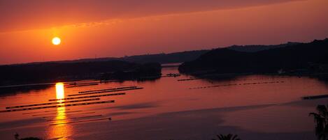 A sunset over a calm body of water with boats and distant hills.