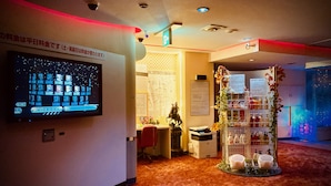 Een hotellobby met een digitaal scherm, een receptiebalie, een beeld en een bloemstuk.