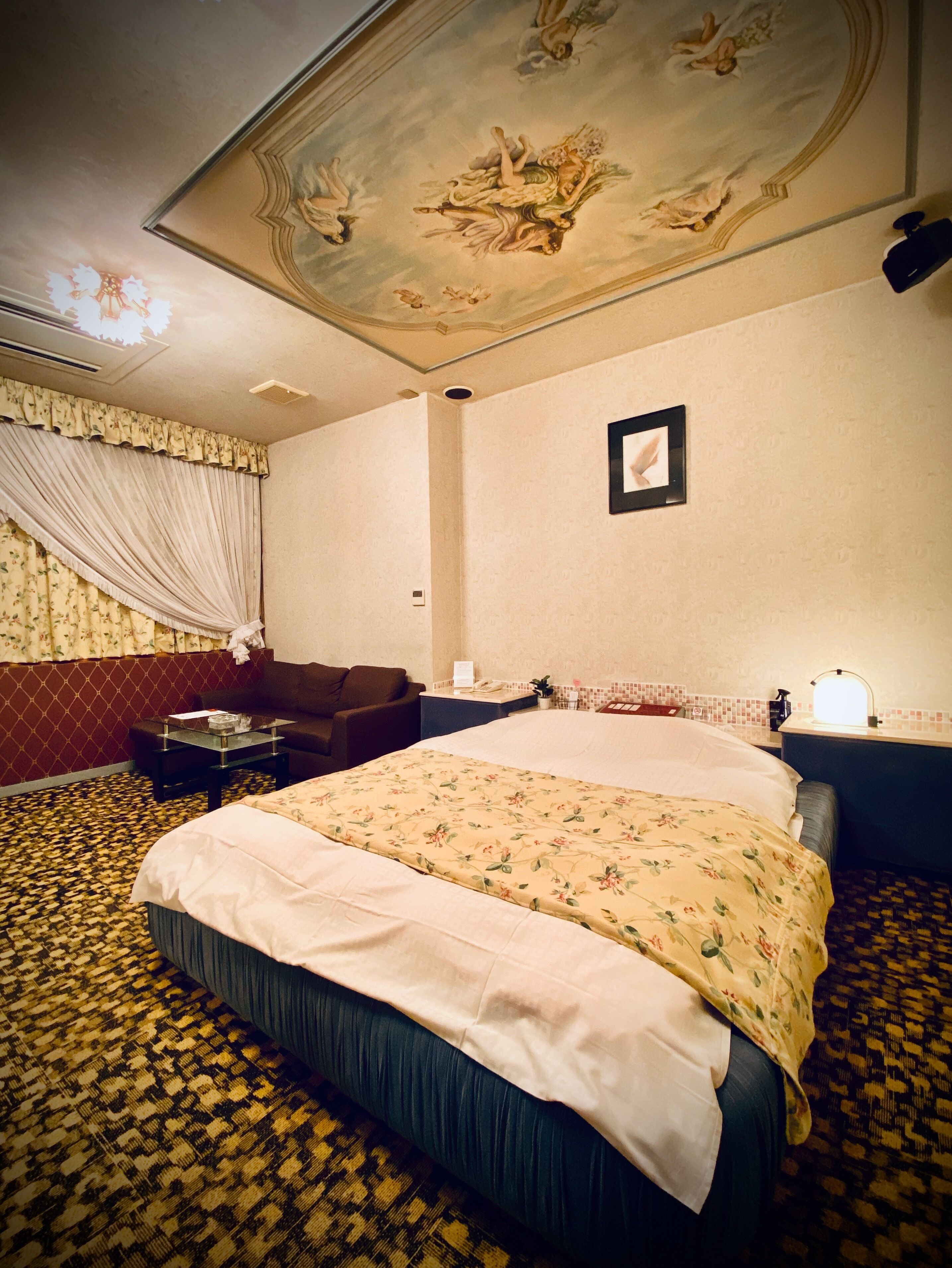 A hotel room with a large bed, a sofa, a small table, and a nightstand.