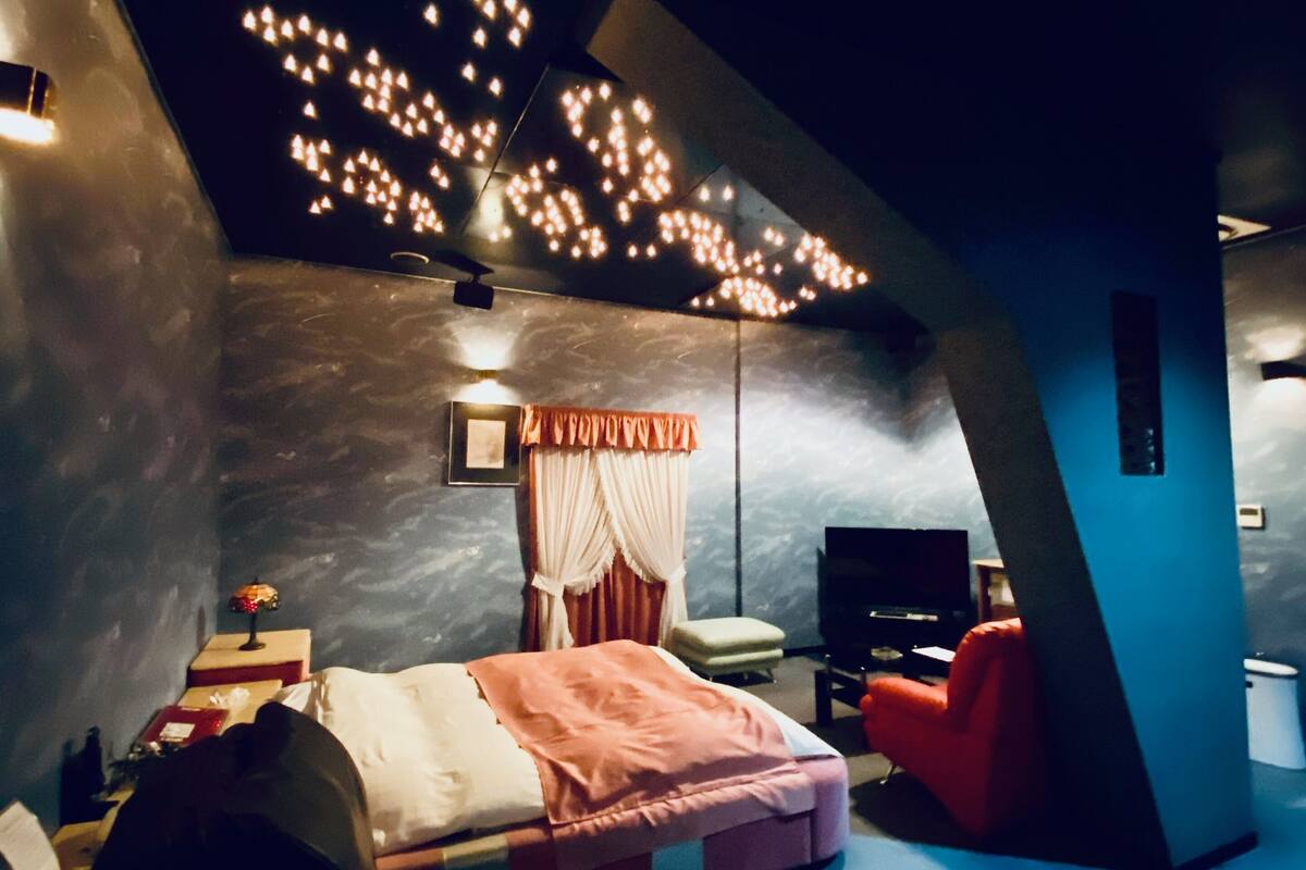 Un dormitorio moderno con cama, sofá rojo, televisor y lámpara en el techo.