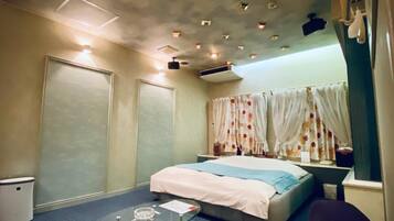 A hotel room with a bed, a small table with a glass top, a chair, and a window with curtains.