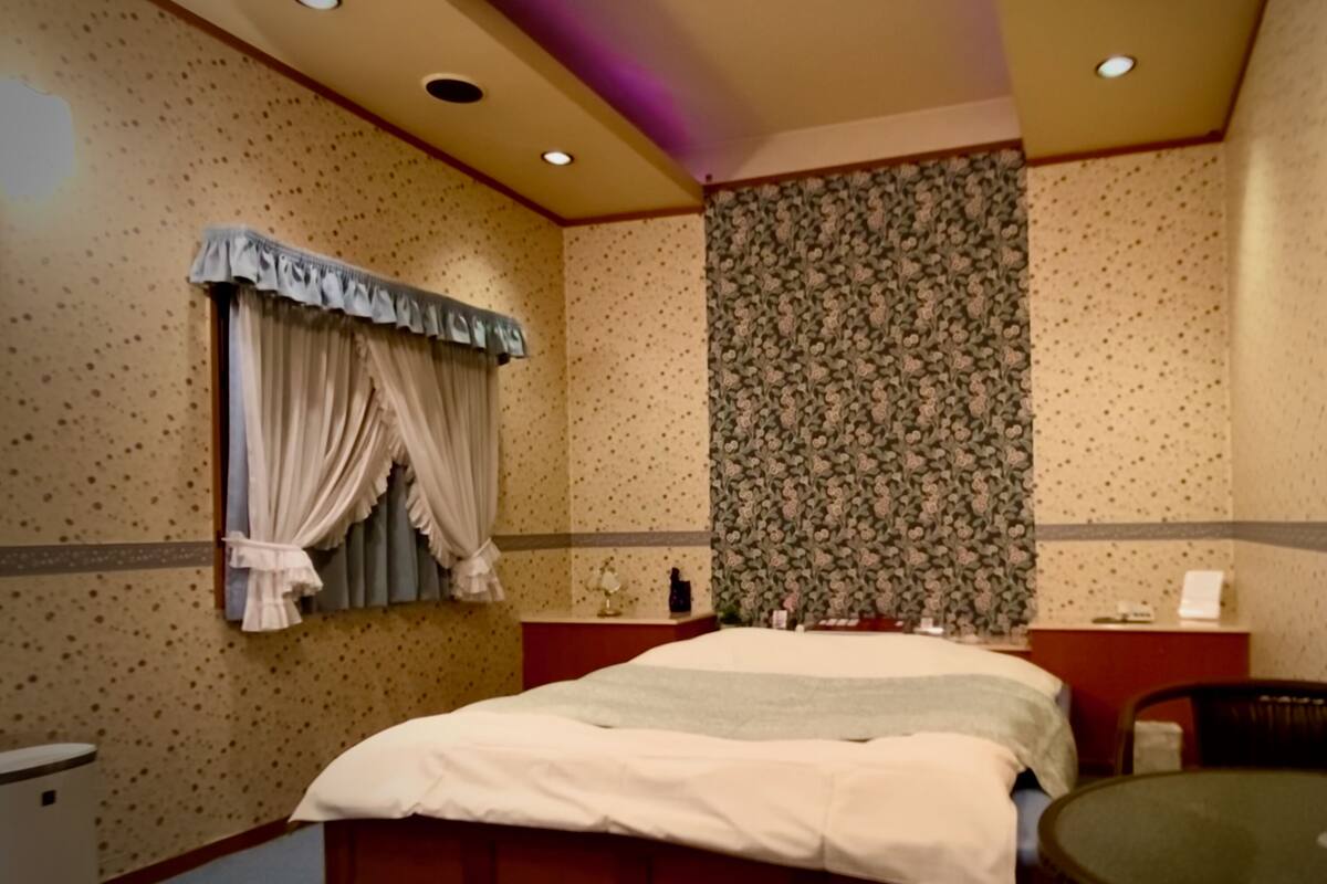 Una habitación de hotel con cama, una mesita, un espejo y una cortina.