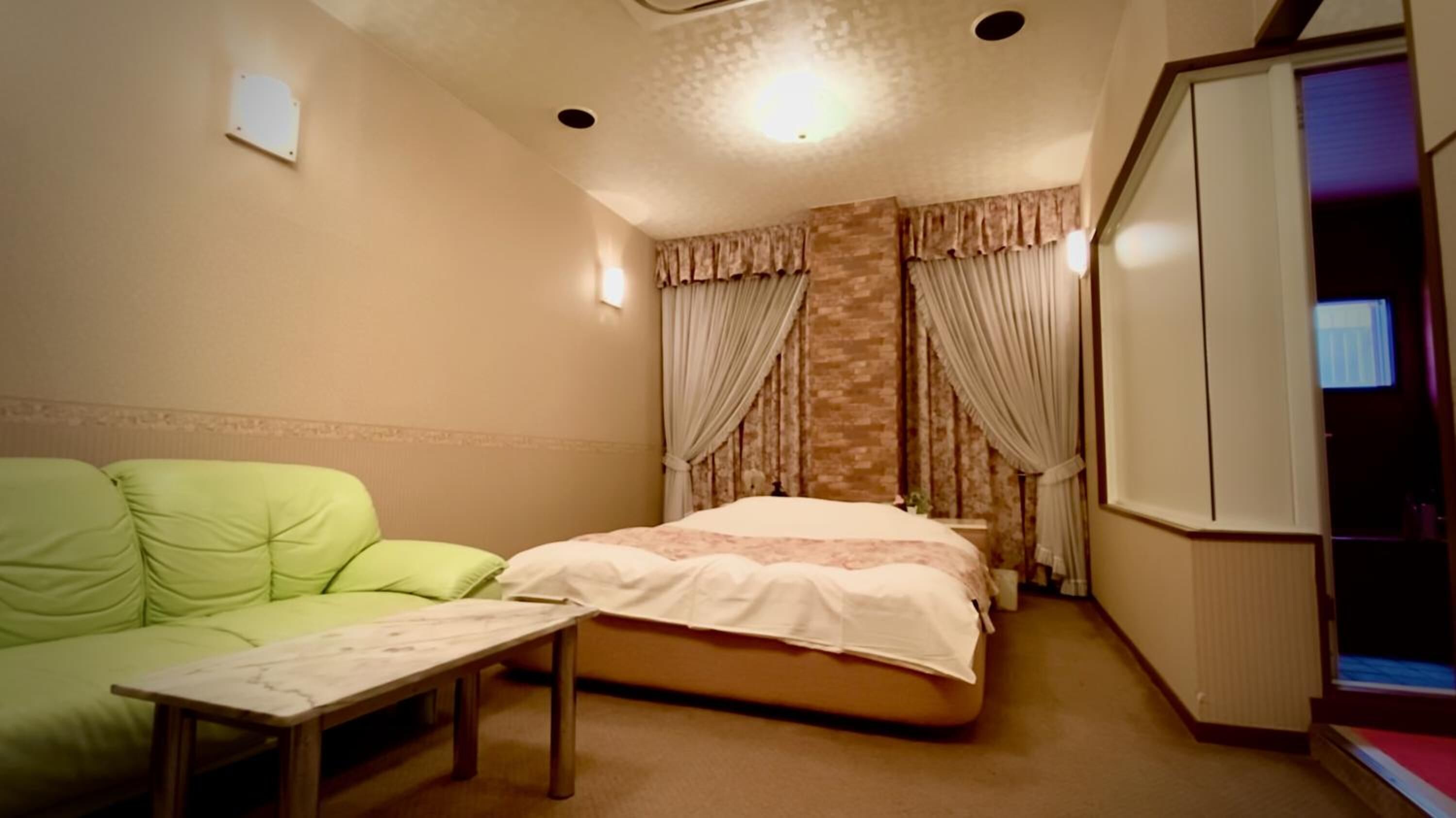 A hotel room with a bed, a green sofa, a small table, and a wardrobe.