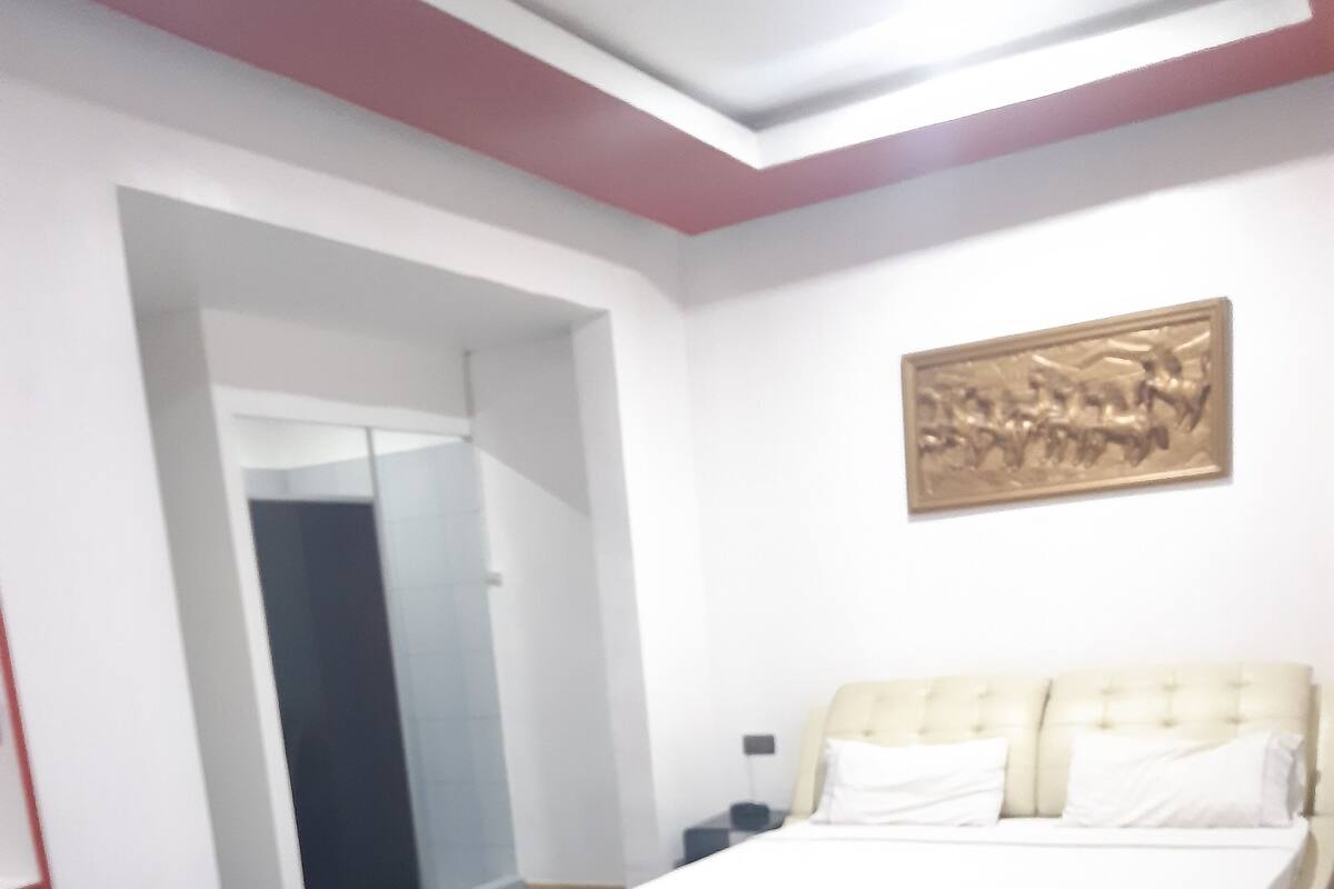 Una camera d'albergo con un letto, un tavolino in vetro, una sedia marrone e un quadro appeso al muro.