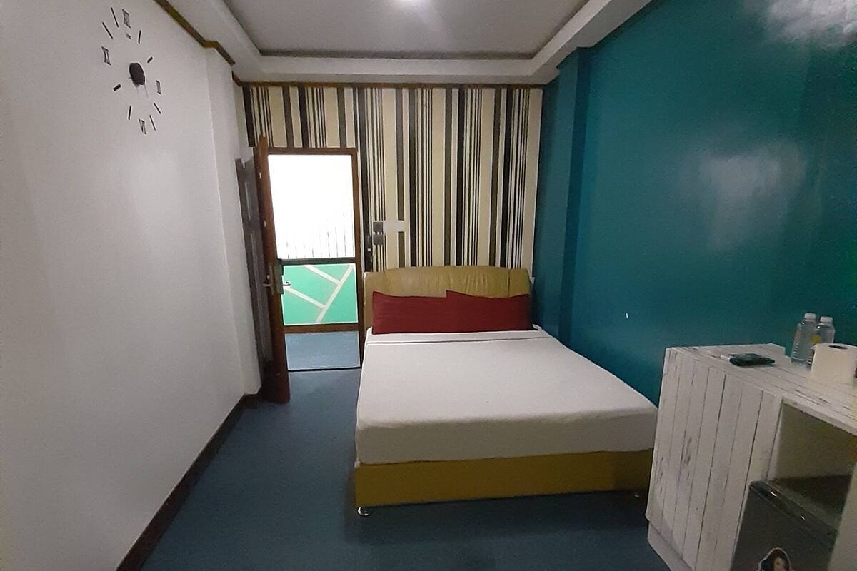 Una stanza con un letto, una scrivania, una sveglia e vista su un campo sportivo.