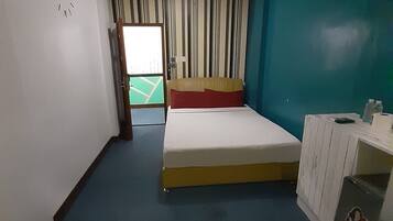 Een kamer met een bed, een bureau, een klok en uitzicht op een sportveld.