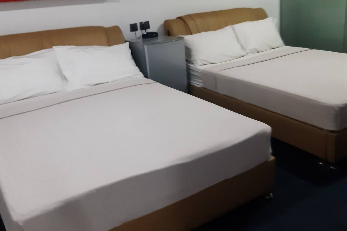 Una camera d'albergo con due letti, una parete decorata in rosso e una porta verde.