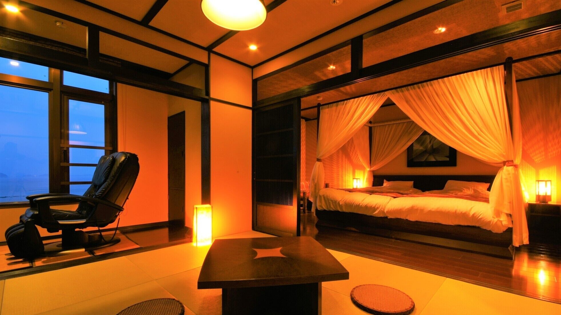 A room with a bed, a chair, a table, and a view of the sea.