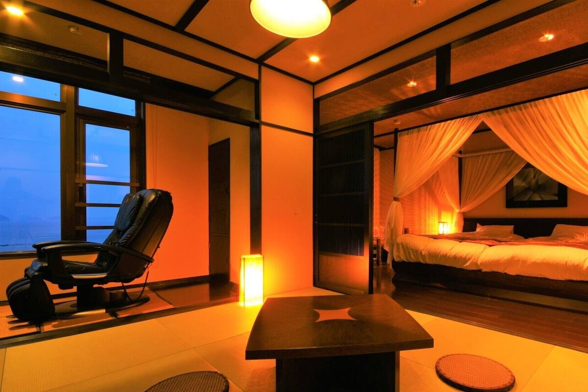 A room with a bed, a chair, a table, and a view of the sea.