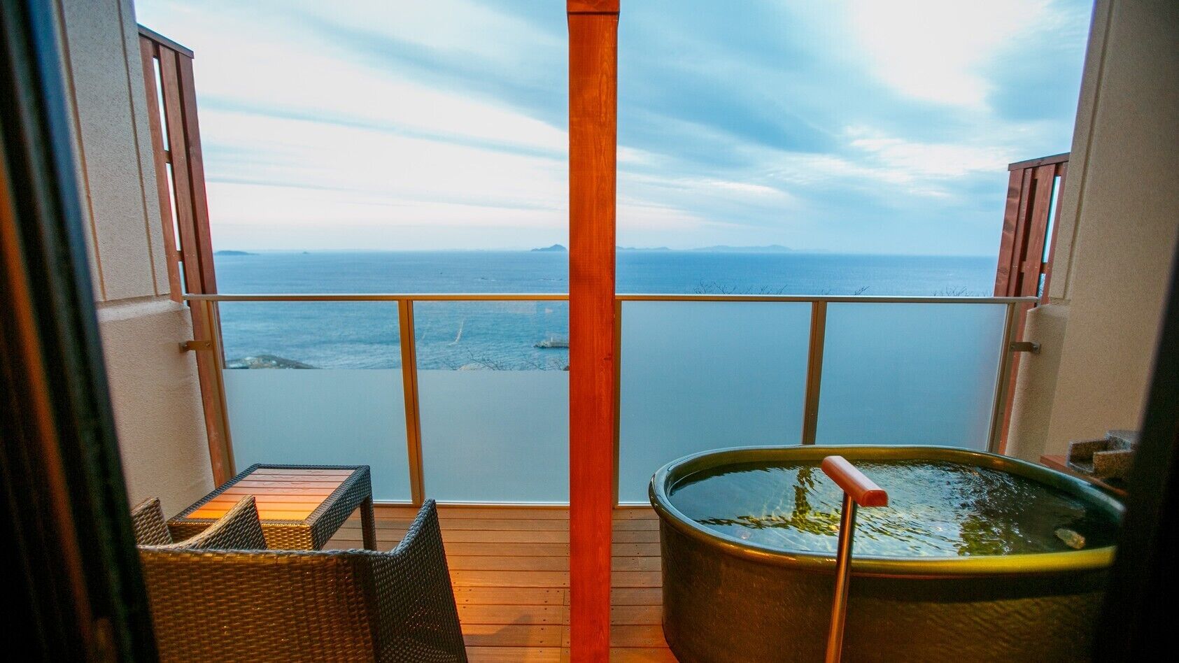 A balcony with a view of the sea, a hot tub, and wicker furniture.