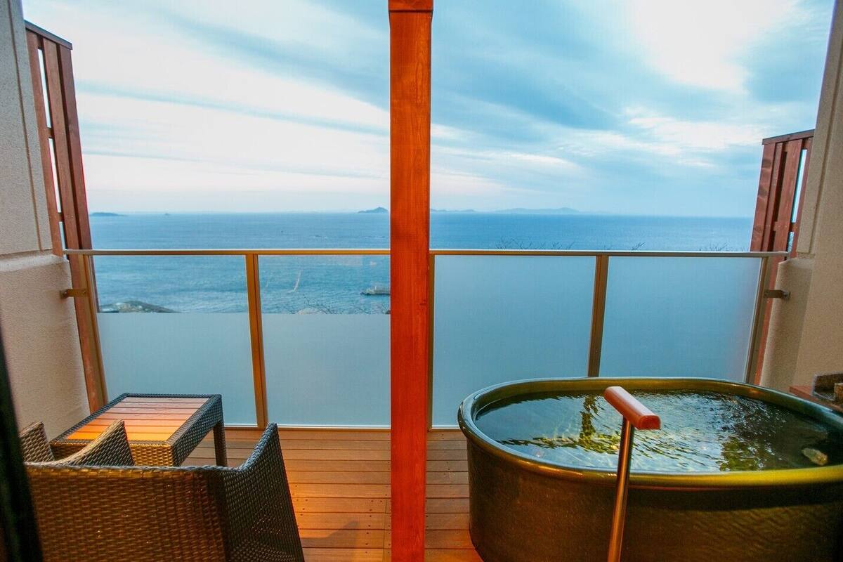A balcony with a view of the sea, a hot tub, and wicker furniture.