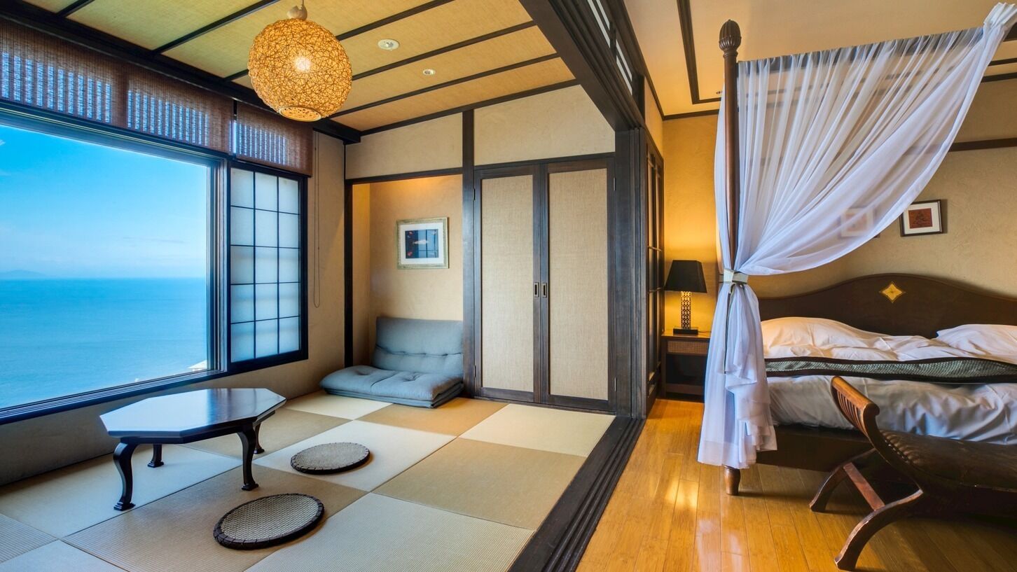 A traditional Japanese-style room with tatami flooring, a low table, a cushioned seating area, a bed with a canopy, and a view of the sea.