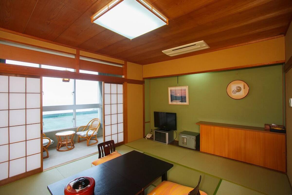 A traditional Japanese-style room with tatami flooring, a low table, and sliding doors leading to a balcony with a view of the sea.