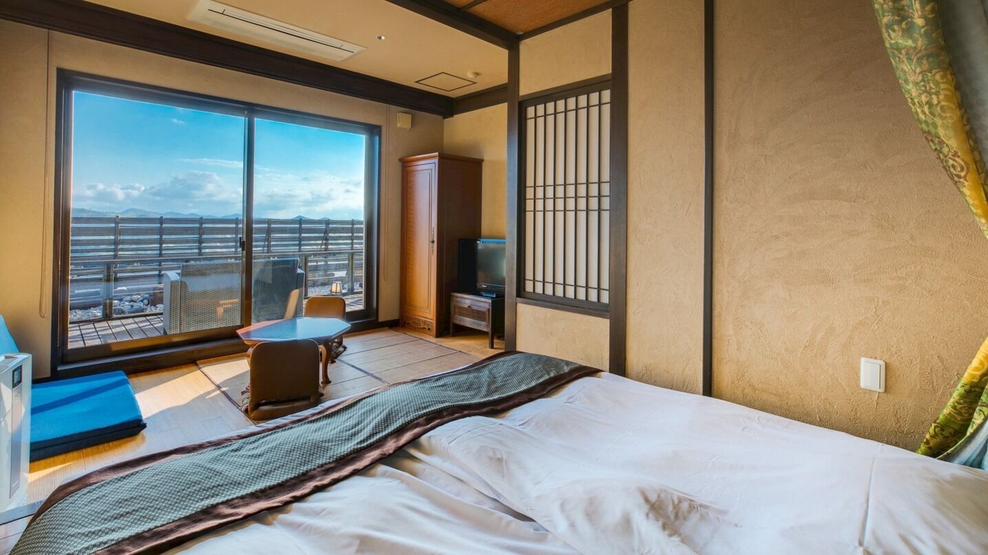 A hotel room with a large sliding glass door, a bed, a small table, a chair, and a television.