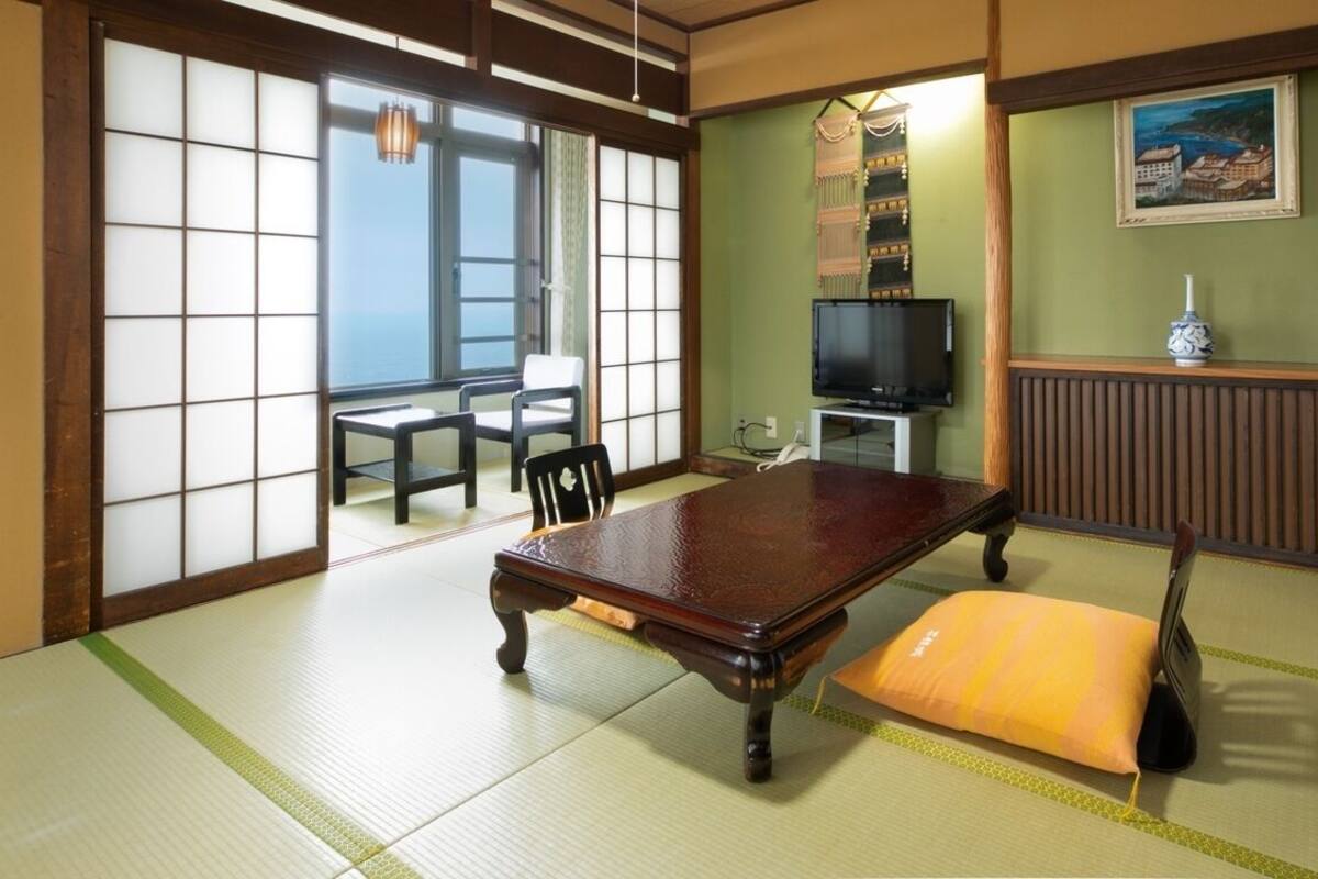 A tatami mat room with a tatami mat table, a television, and a traditional Japanese painting.