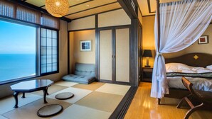 A traditional Japanese-style room with tatami flooring, a low table, a cushioned bench, a bed with a canopy, and a view of the sea. - Ijika Daiichi Hotel Kagura (Toba)