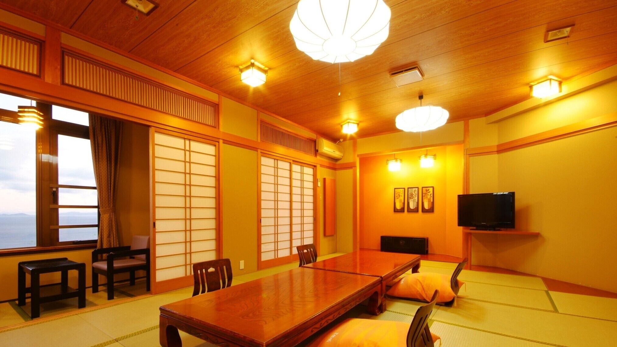 A traditional Japanese room with tatami flooring, a low table, chairs, sliding doors, and a television.