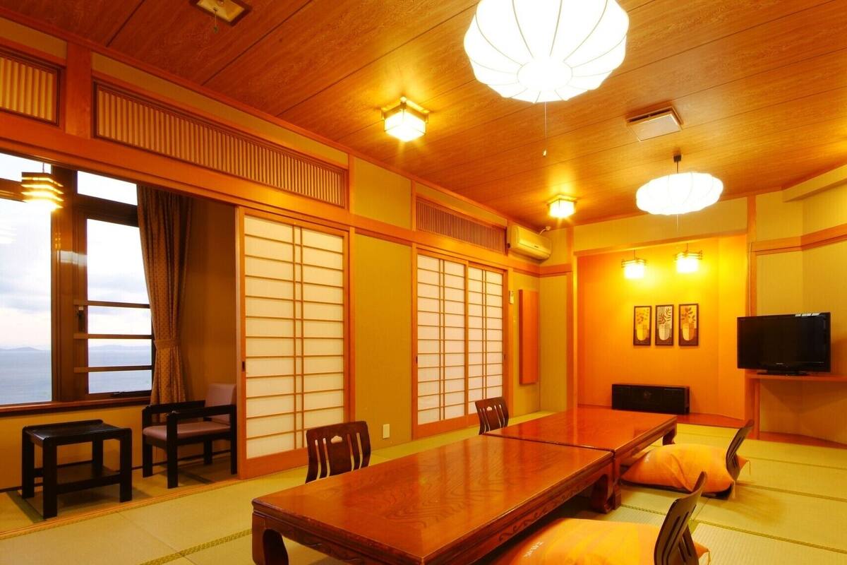 A traditional Japanese room with tatami flooring, a low table, chairs, sliding doors, and a television.