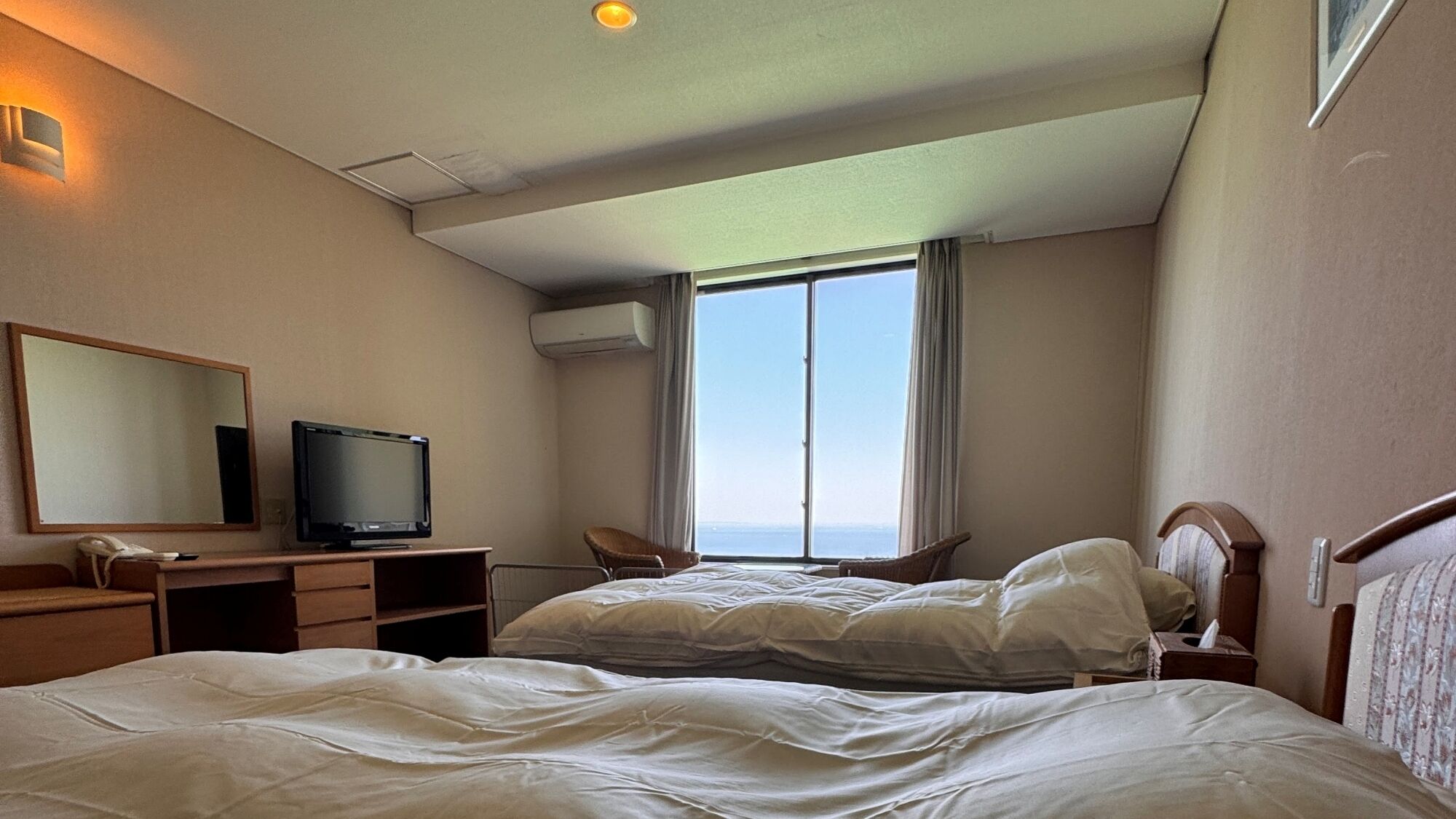 A hotel room with a bed, a desk with a television, a chair, and a large window.