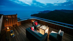 A wooden deck with outdoor furniture, including a sofa and chairs, overlooking a coastal landscape with hills and the sea. - Ijika Daiichi Hotel Kagura (Toba)